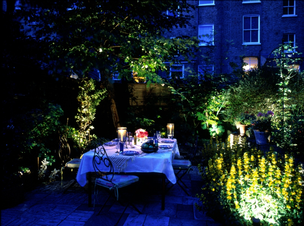 Dining table in garden with softly lit planting