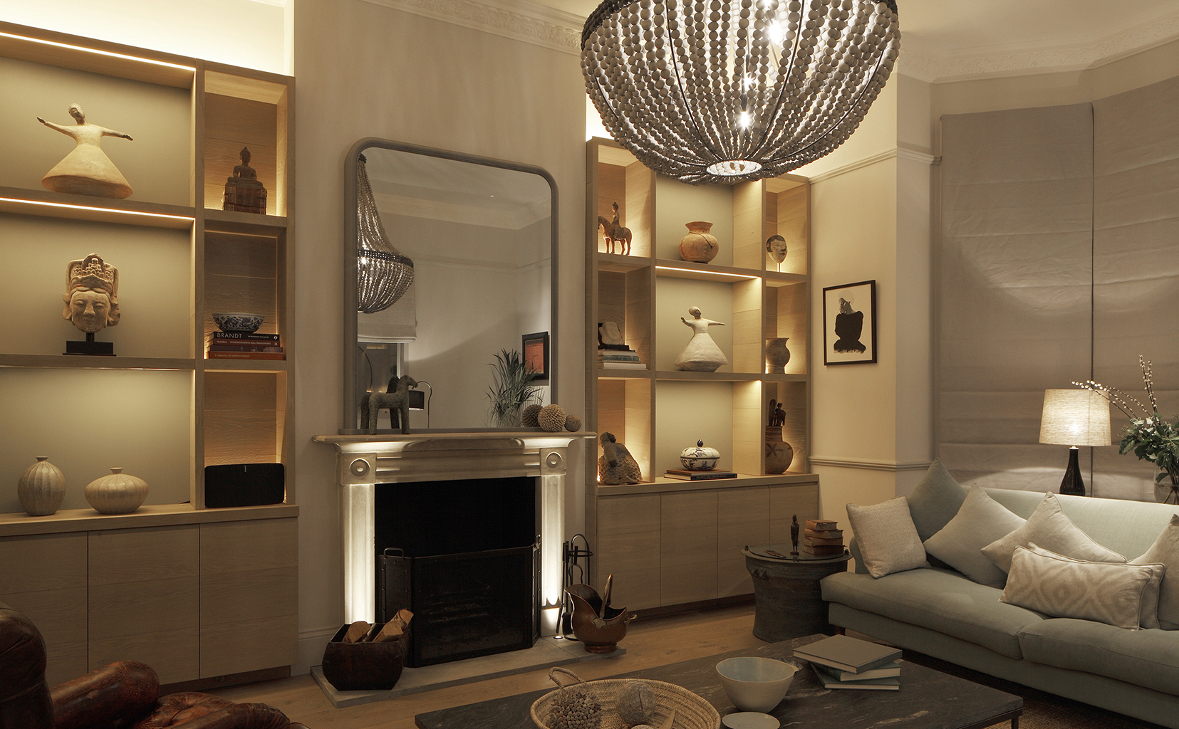 Living room with large pendant layered with table lights next to lit joinery