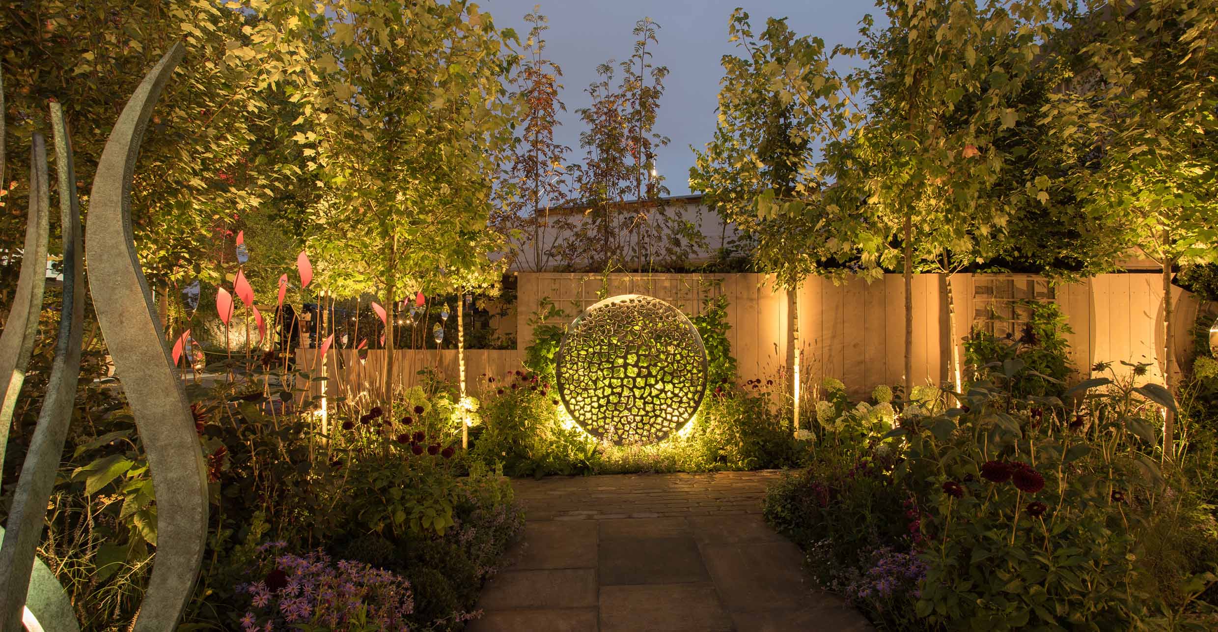 garden with path to dramatic lit sculpture and planting