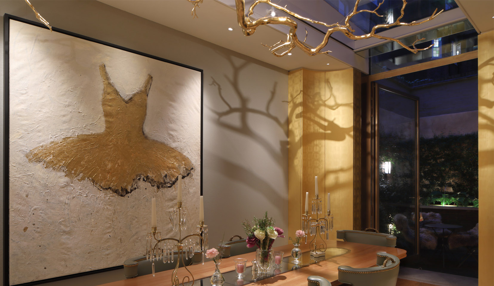 Intricate suspended sculpture hanging above dining table, with artwork on wall and lighting from spotlights