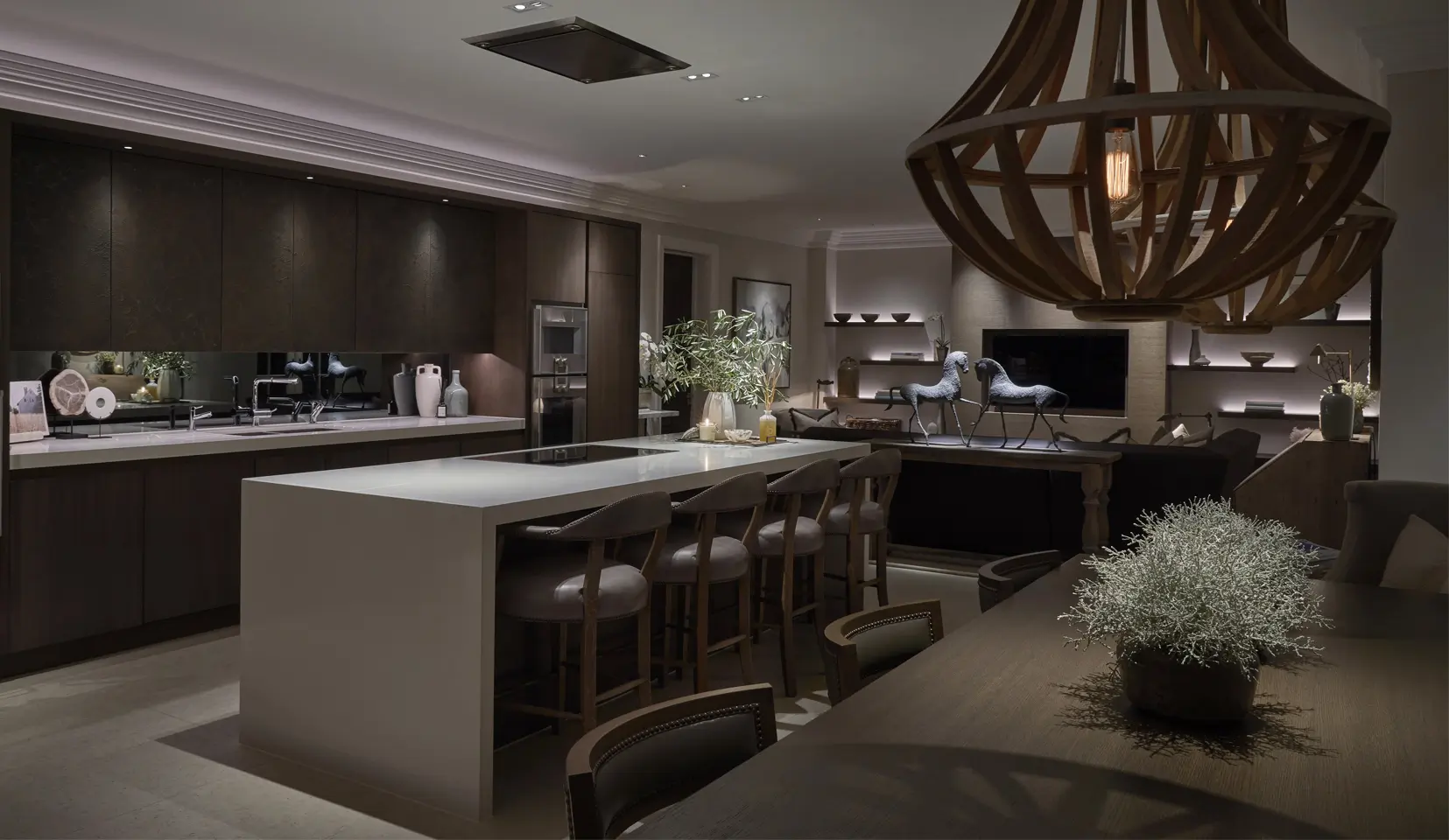 kitchen and seating area with oversized wooden pendants and downlights onto kitchen island, with lit shelves in background