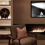 close up detail of backlit shelving with books and objects with armchair and fireplace