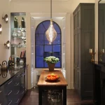 Kitchen with pendant and downlights over the island with shutterboxes lit with uplights in window