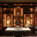 Dark green study with rich wooden joinery unit with lighting to backlight objects and books on shelves