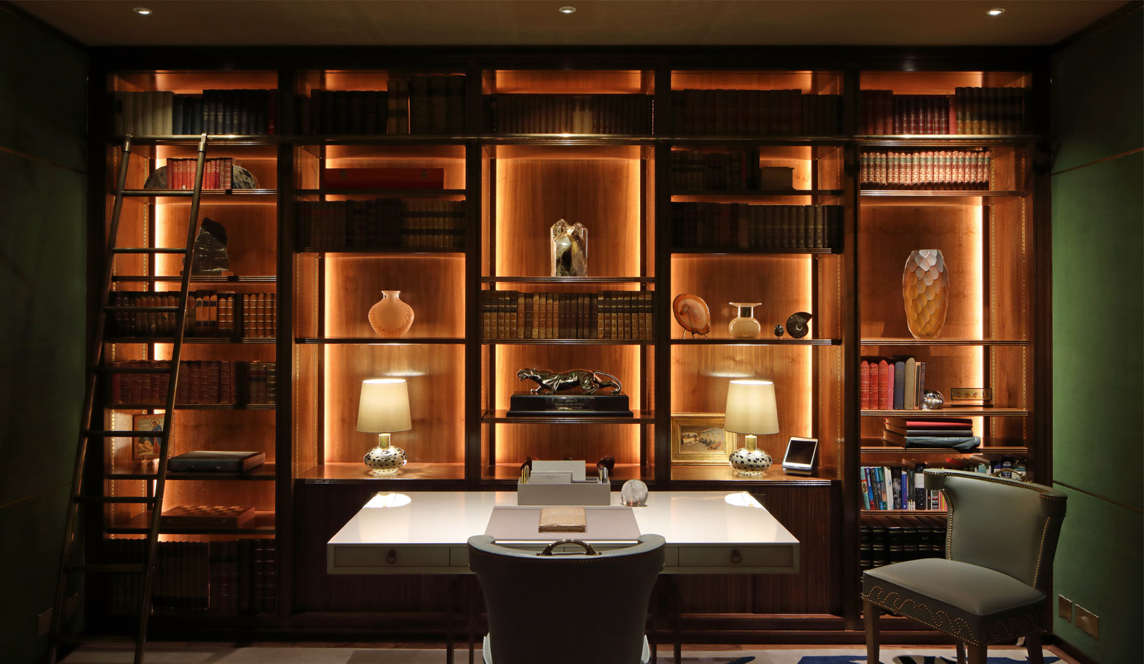 Dark green study with rich wooden joinery unit with lighting to backlight objects and books on shelves