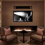 Mid century townhouse living room with fireplace and armchairs, with lit shelving either side