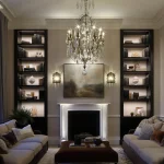 Grade listed building living room with lit joinery shelving either side of fireplace and hanging chandelier in centre