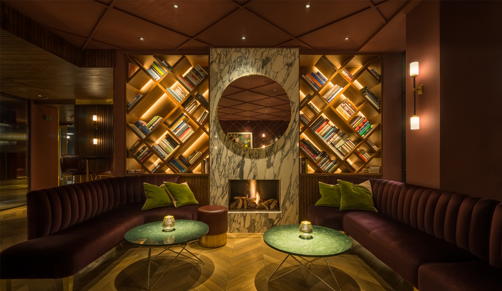 lit shelving units either side of fireplace in cosy bar with sofas and coffee tables