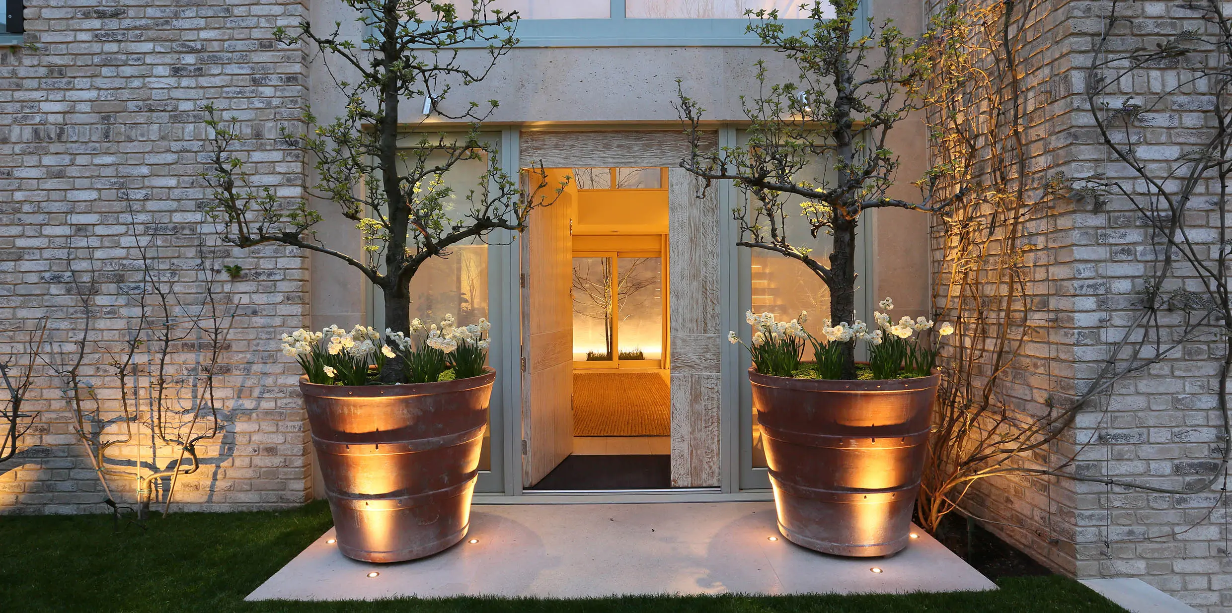 over sized pots with planting and uplights frame a contemporary front door with