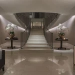 grand entrance hall with sweeping staircase with linear light underneath and orchids on tables either side