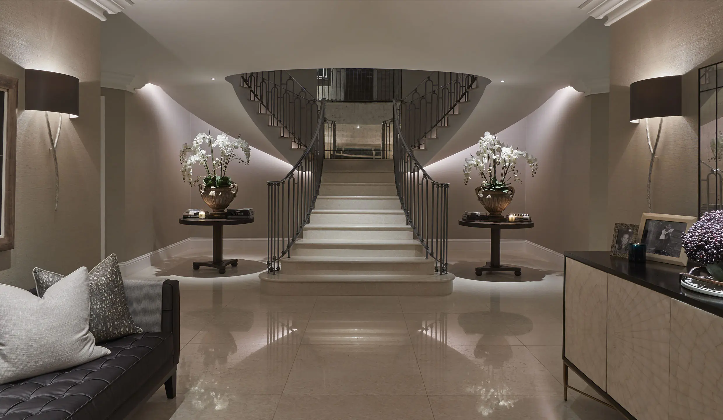 grand entrance hall with sweeping staircase with linear light underneath and orchids on tables either side