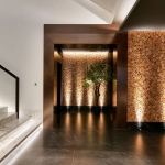 Dramatic Staircase with linear lit steps, leading to hallway with up lighting to textured wooden wall